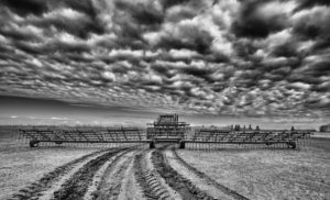 A tractor pulling a harrow bar across a field for spring preparation in rural dramatic black and white landscape
